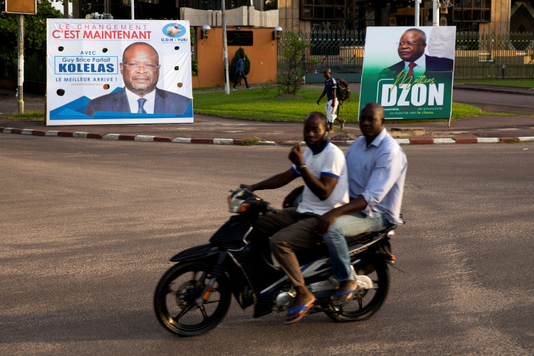 Men on a motorbike ride past billboards of presidential candidates and leading opposition leaders Guy Brice Parfait Kolelas and Mathias Dzon, in Brazzaville, Republic of Congo March 17, 2021 [Hereward Holland/ Reuters]