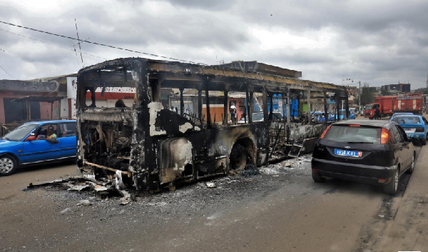 A man drives past a public transport bus which was burned during a protest