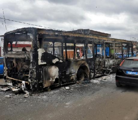 A man drives past a public transport bus which was burned during a protest