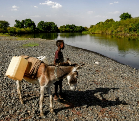 A boy stands next to a donkey loaded with jerry cans by the Atbarah River near the village of Dukouli within the Quraysha locality, located in the Fashaqa al-Sughra agricultural region of Sudan's eastern Gadarif state